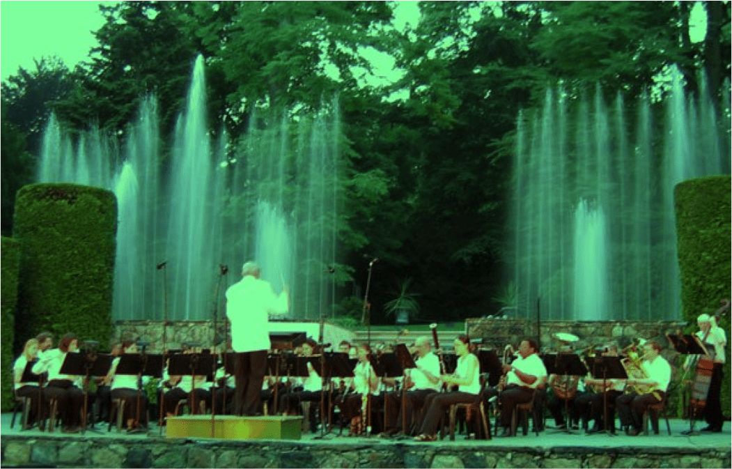 An orchestra playing outside with a fountain background